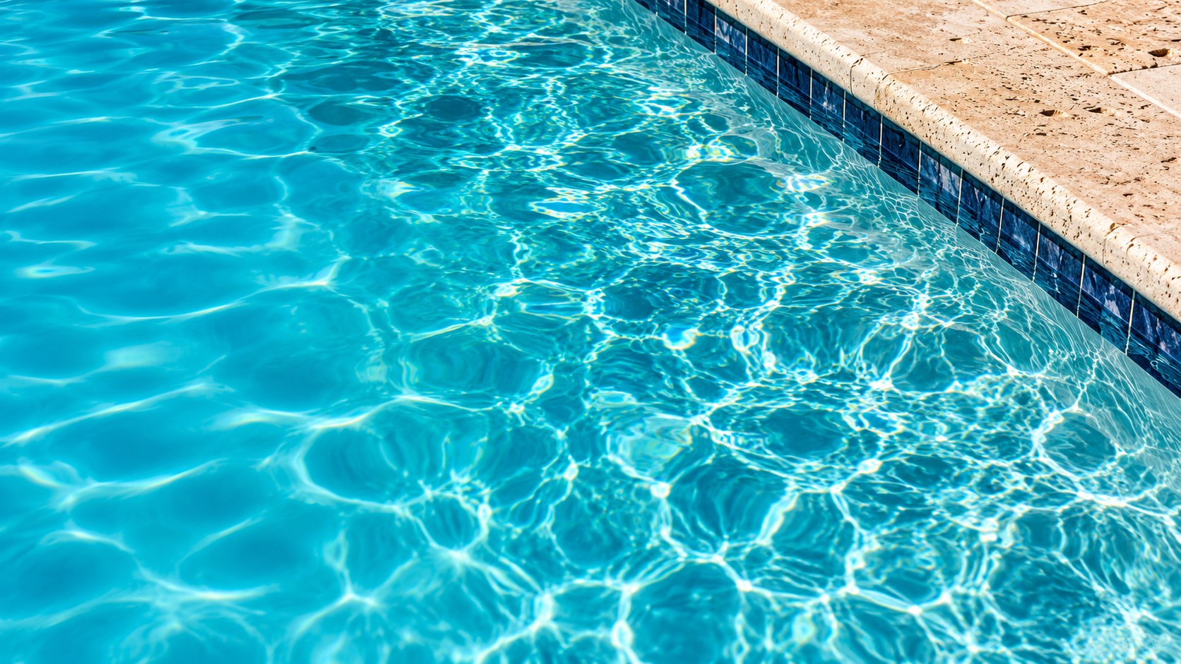 Sunlit turquoise pool water beside a pale stone edge